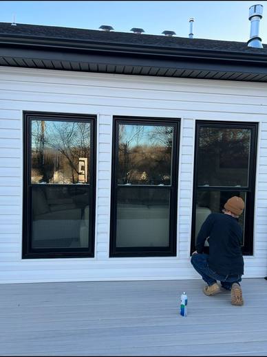 Technician cleaning three new black double-hung windows on white siding