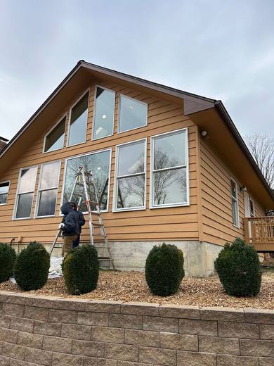 Crew on a ladder working on the large gable windows of a tan-sided house