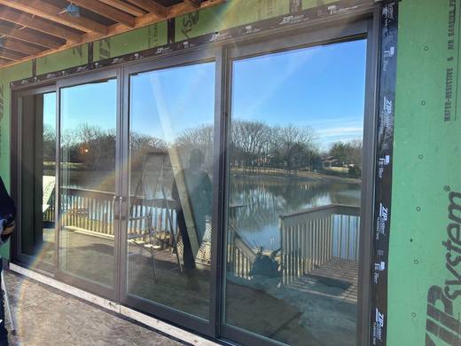 Multi-panel sliding glass door reflecting a lake, on a home under construction