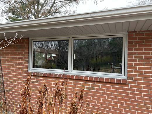 Two sliding windows with white frames on a brick ranch house